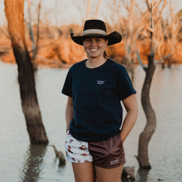Person wearing a hat standing by a body of water with trees in the background