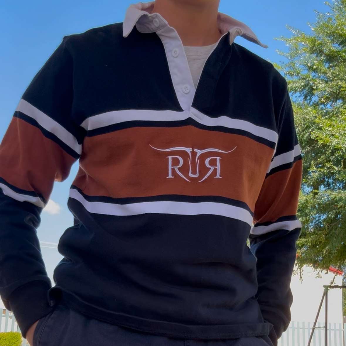 Person wearing a rugby-style shirt with 'RJA' logo outdoors.
