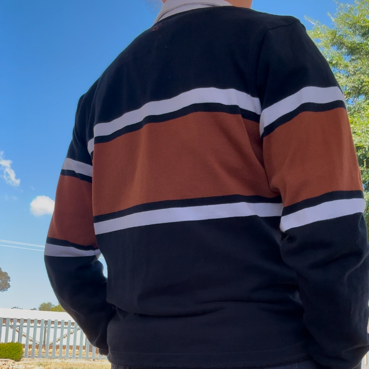 Person wearing a striped sweater and shorts standing outdoors with a clear sky.