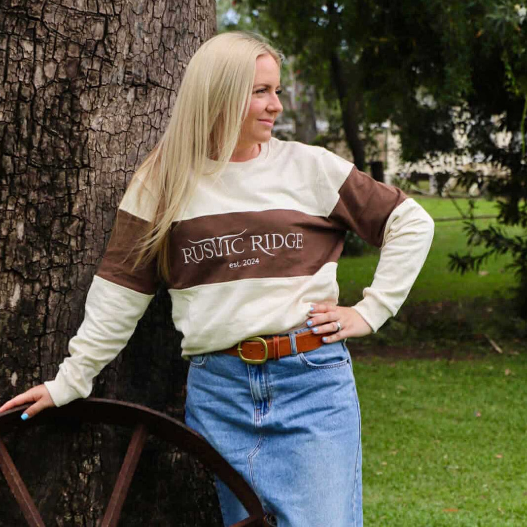 Woman wearing a striped sweater and jeans leaning against a tree in a park.
