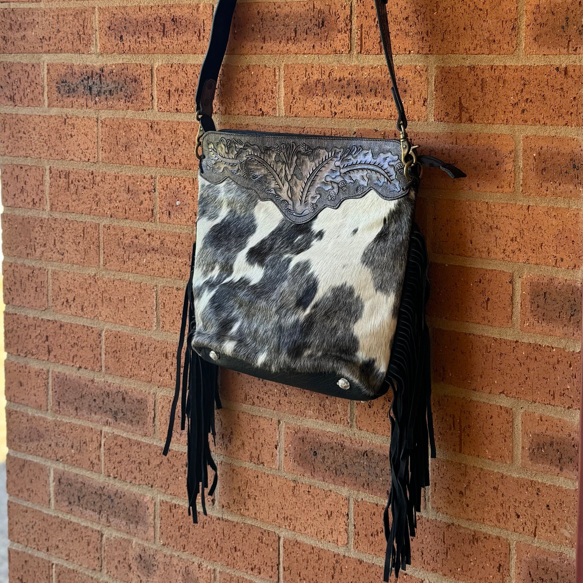 Black and white patterned handbag with fringes hanging on a brick wall.