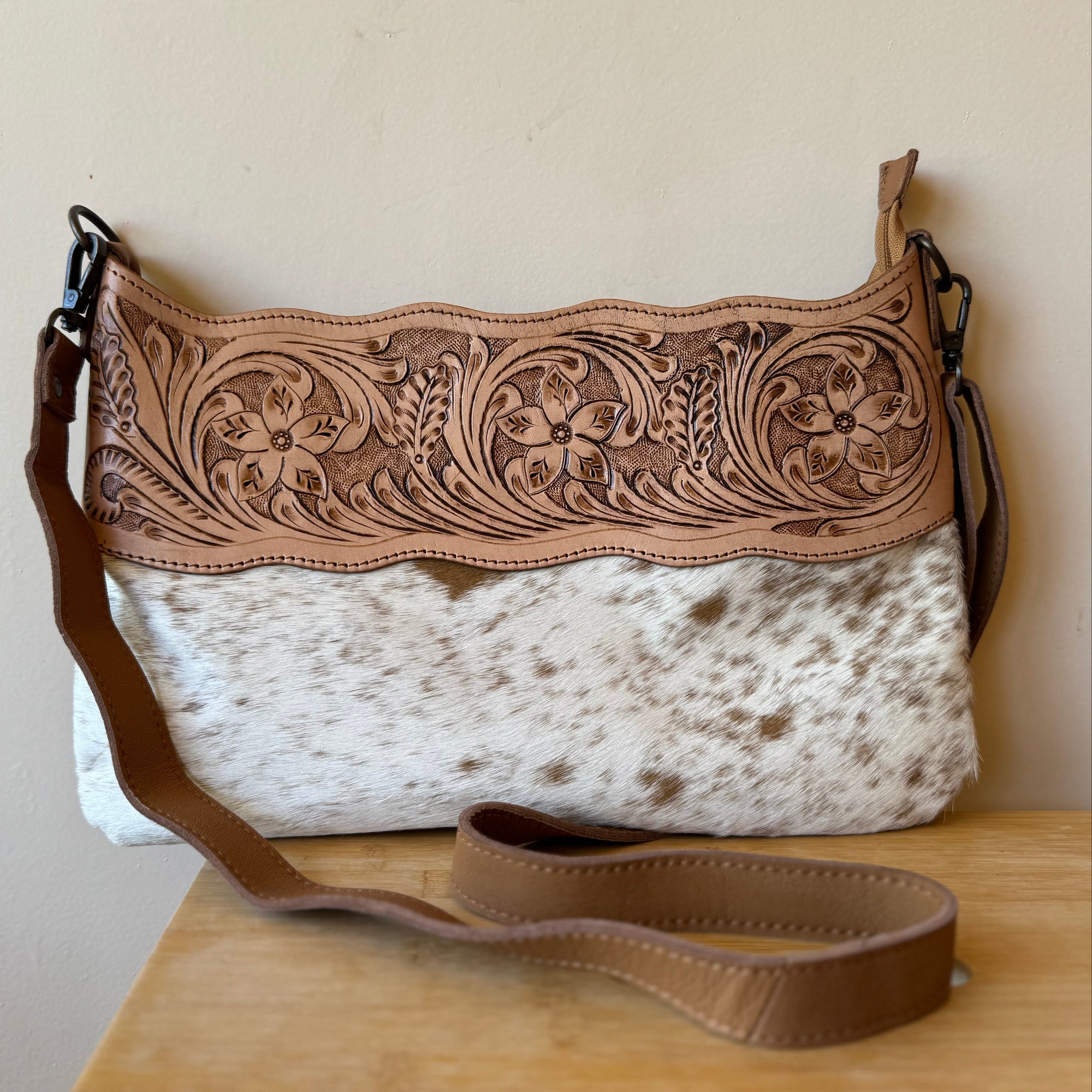 Handbag with floral tooled leather top and cowhide pattern base on a wooden surface.