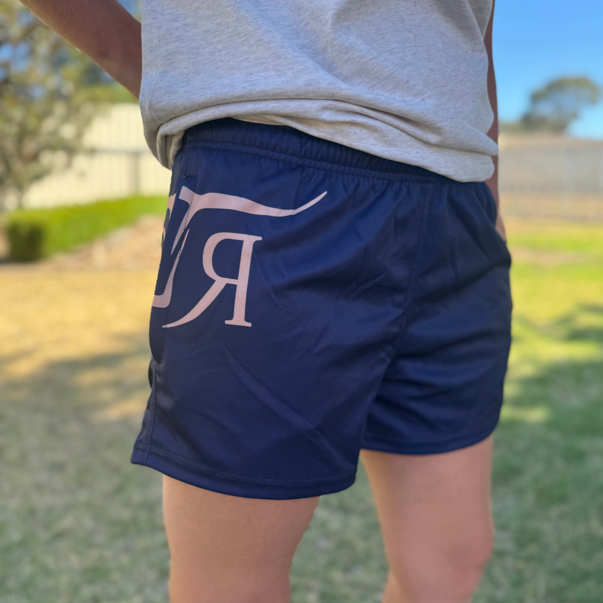 Person wearing blue shorts with a logo, standing outdoors.
