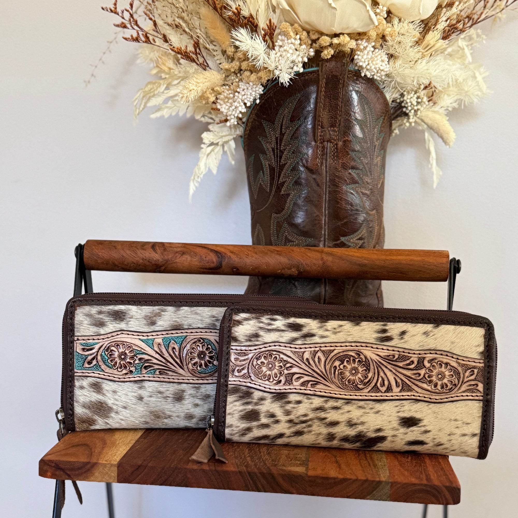 Two cowhide leather wallets with intricate designs on a wooden chair.