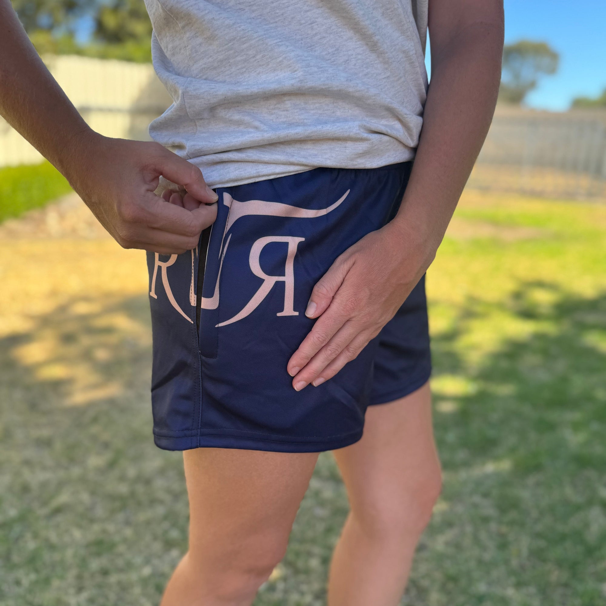 Person wearing navy shorts with a logo, standing outdoors on grass.