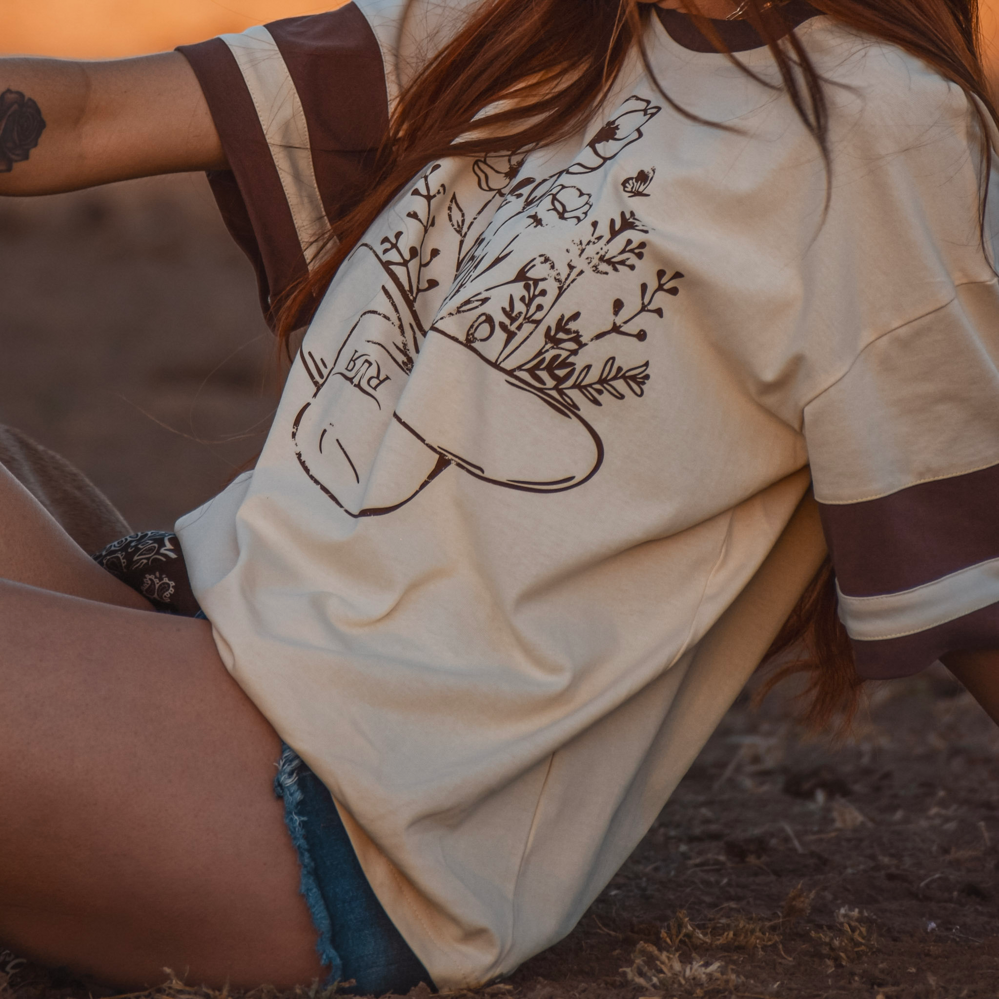 Person wearing a beige t-shirt with a nature-themed design, sitting outdoors.