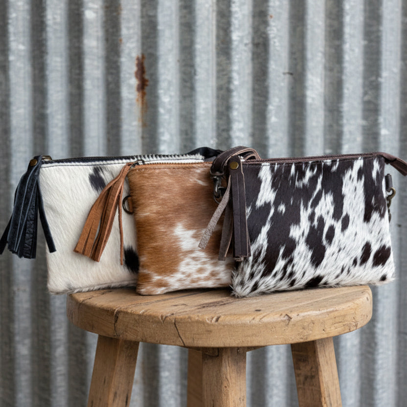 Three cowhide bags with black, white, and brown patterns on a wooden stool against a corrugated metal background.