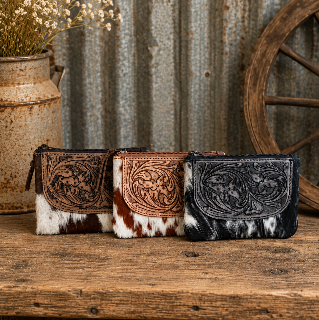 Three cowhide wallets with intricate designs on a wooden surface with rustic background