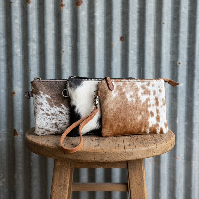 Two cowhide leather bags on a wooden stool against a corrugated metal background