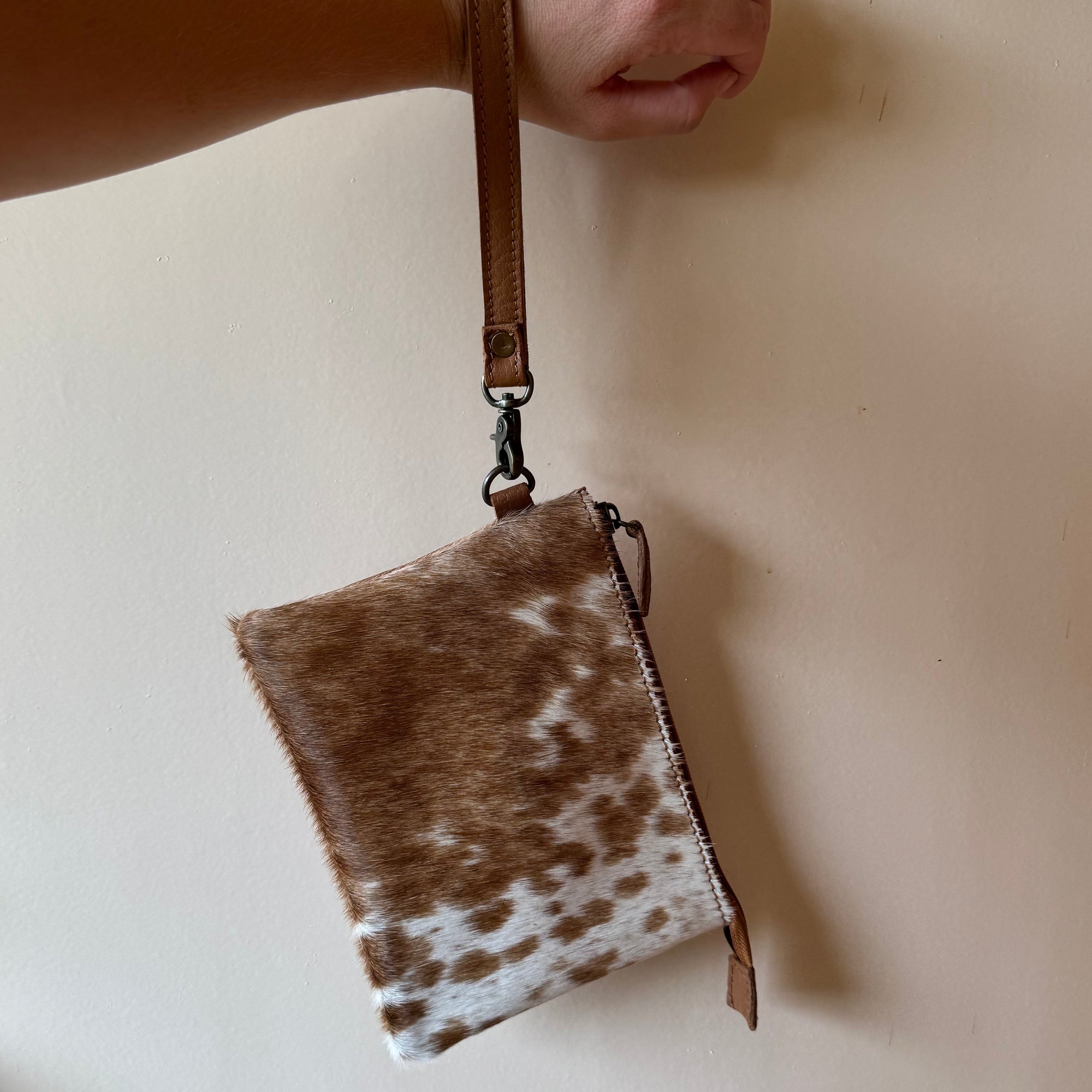 Hand holding a cowhide leather pouch against a plain background
