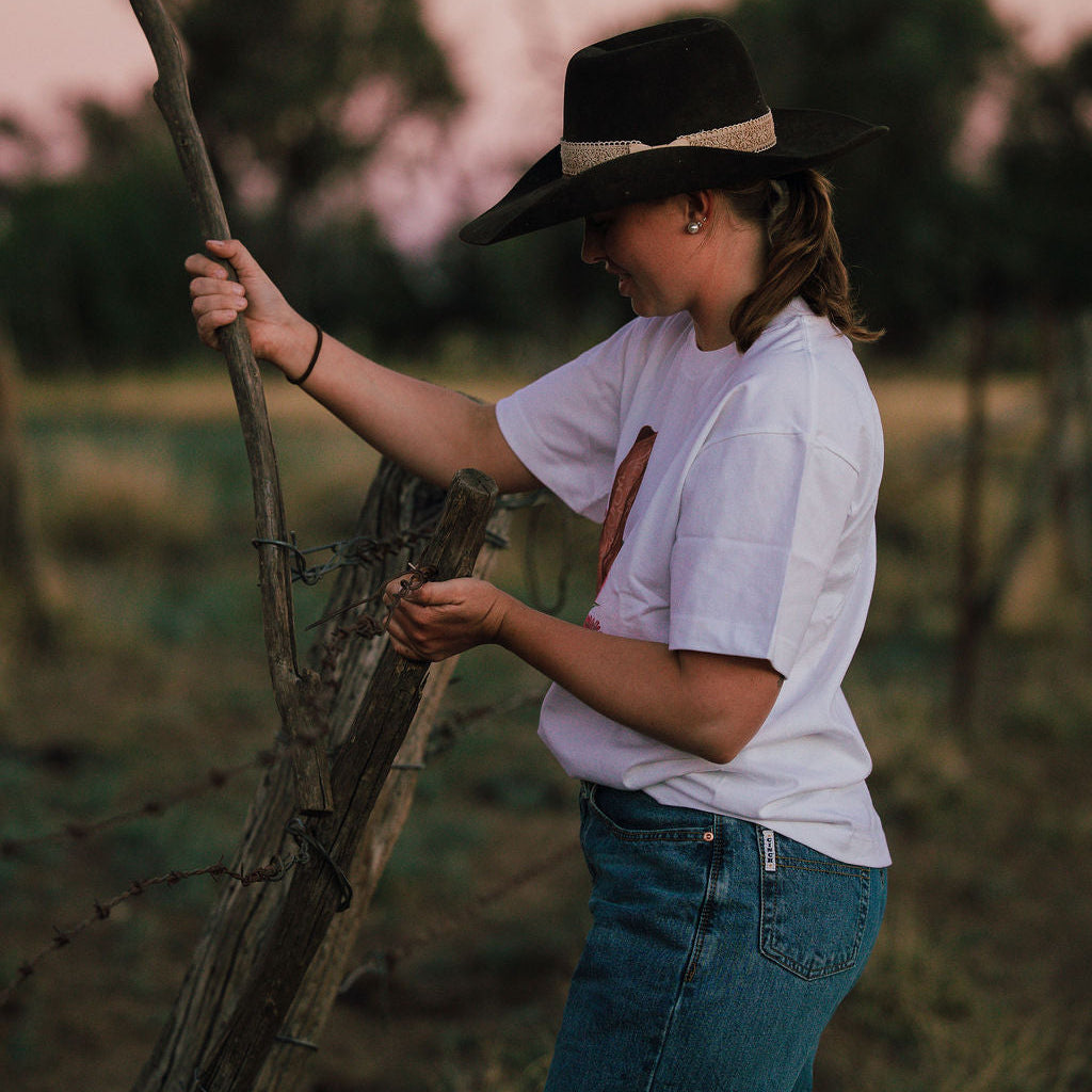 Person wearing a hat and white shirt standing in a field holding a stick.