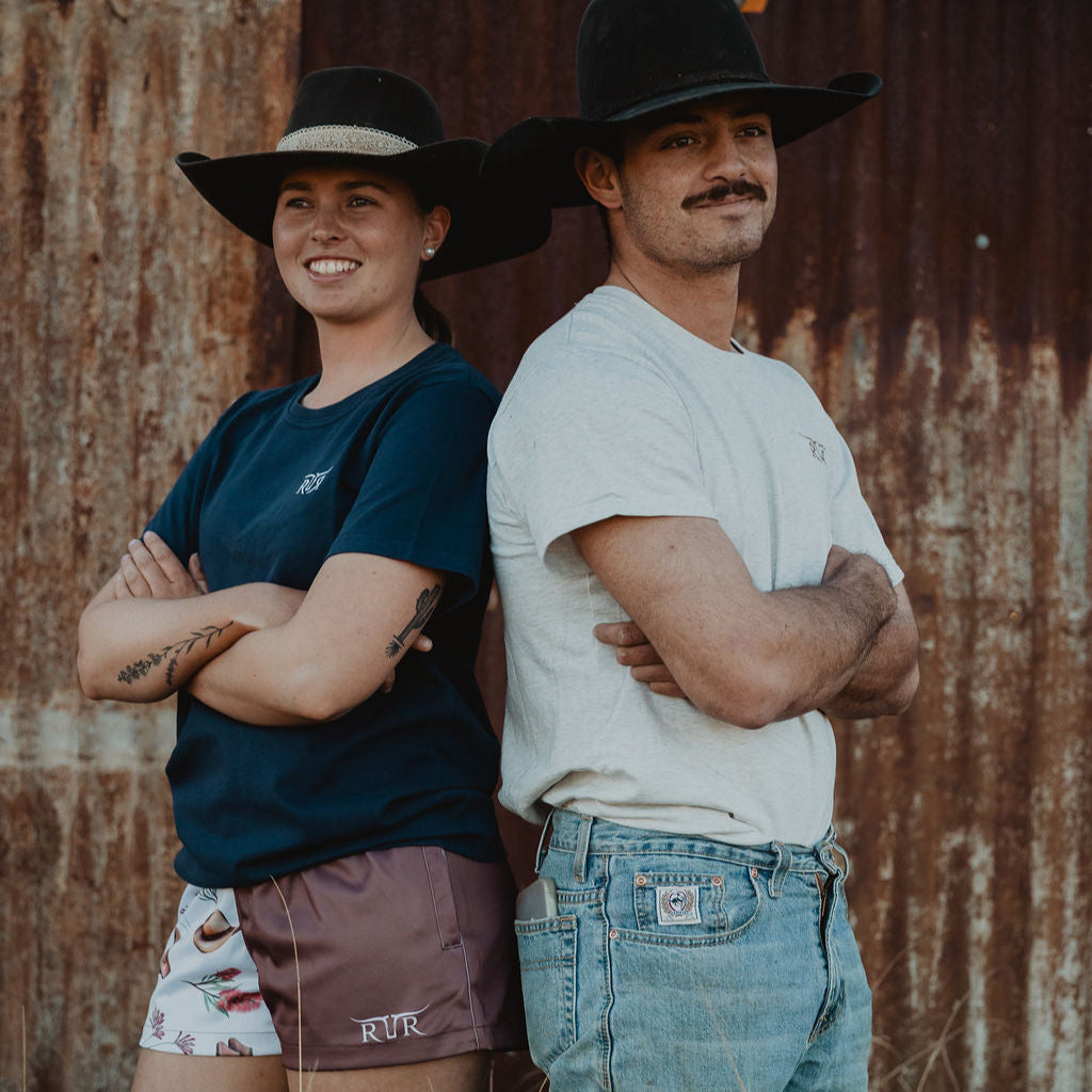 Two people wearing cowboy hats standing in front of a rusted metal wall.