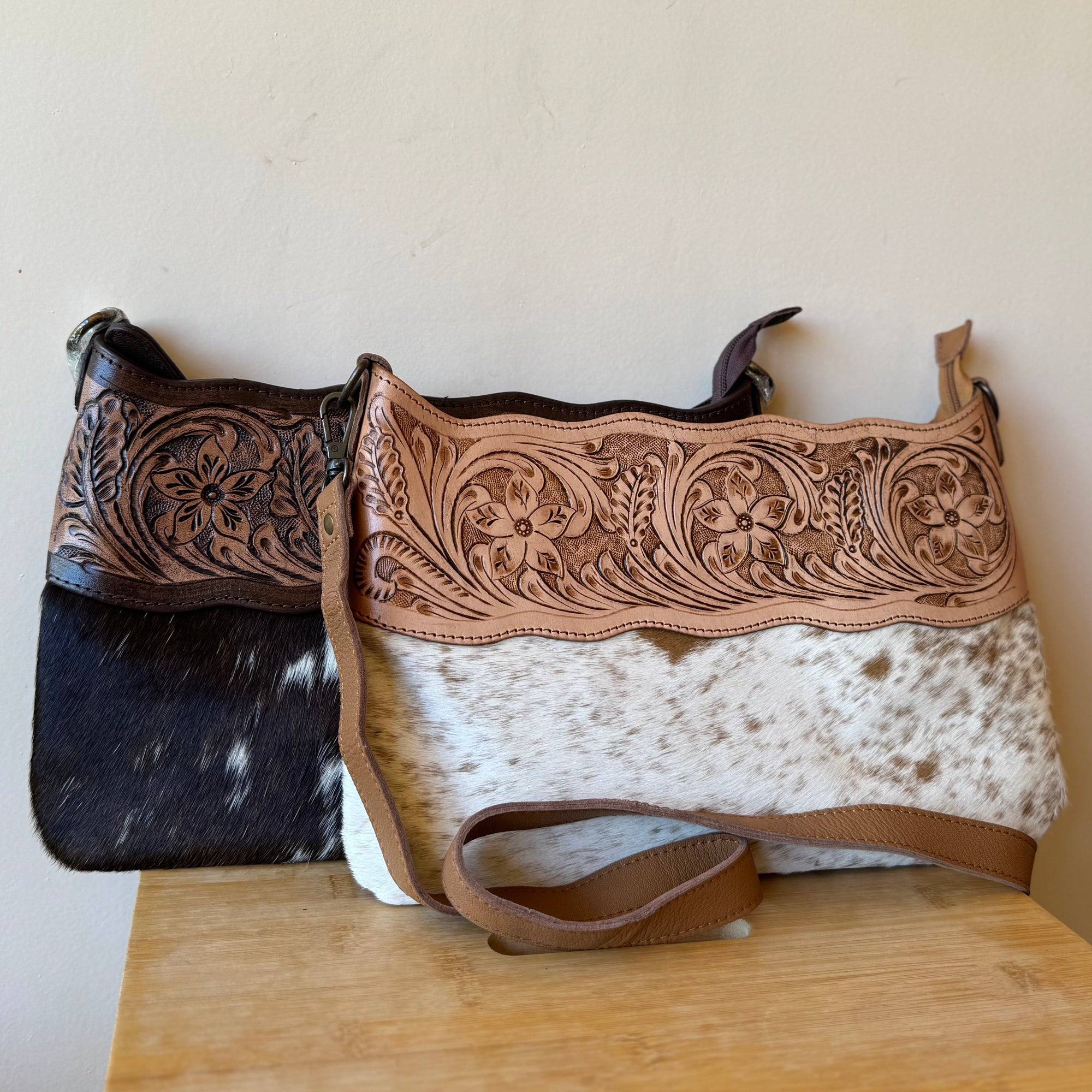 Two handbags with intricate designs on a wooden surface against a plain wall.