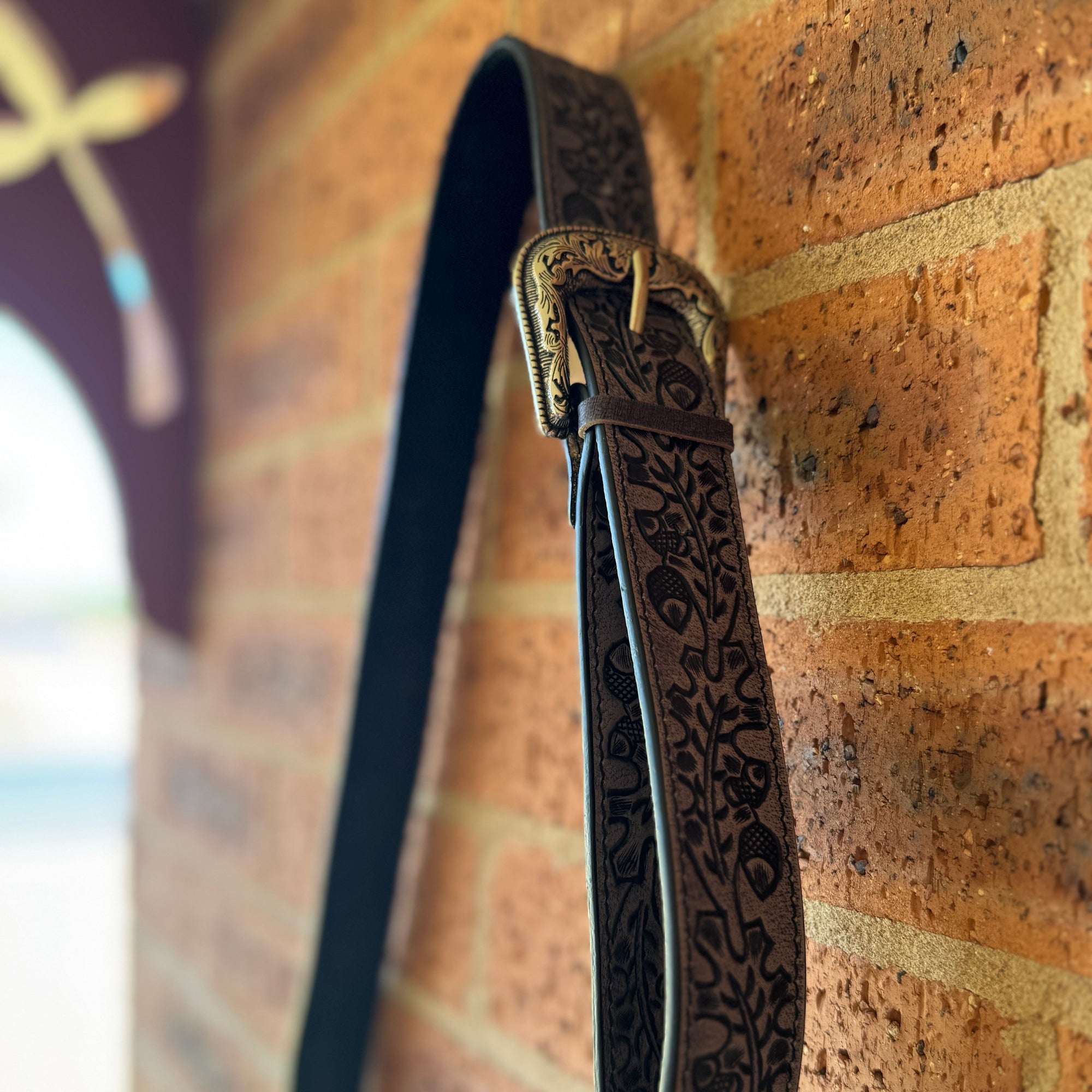 Decorative leather strap with intricate patterns hanging on a brick wall.