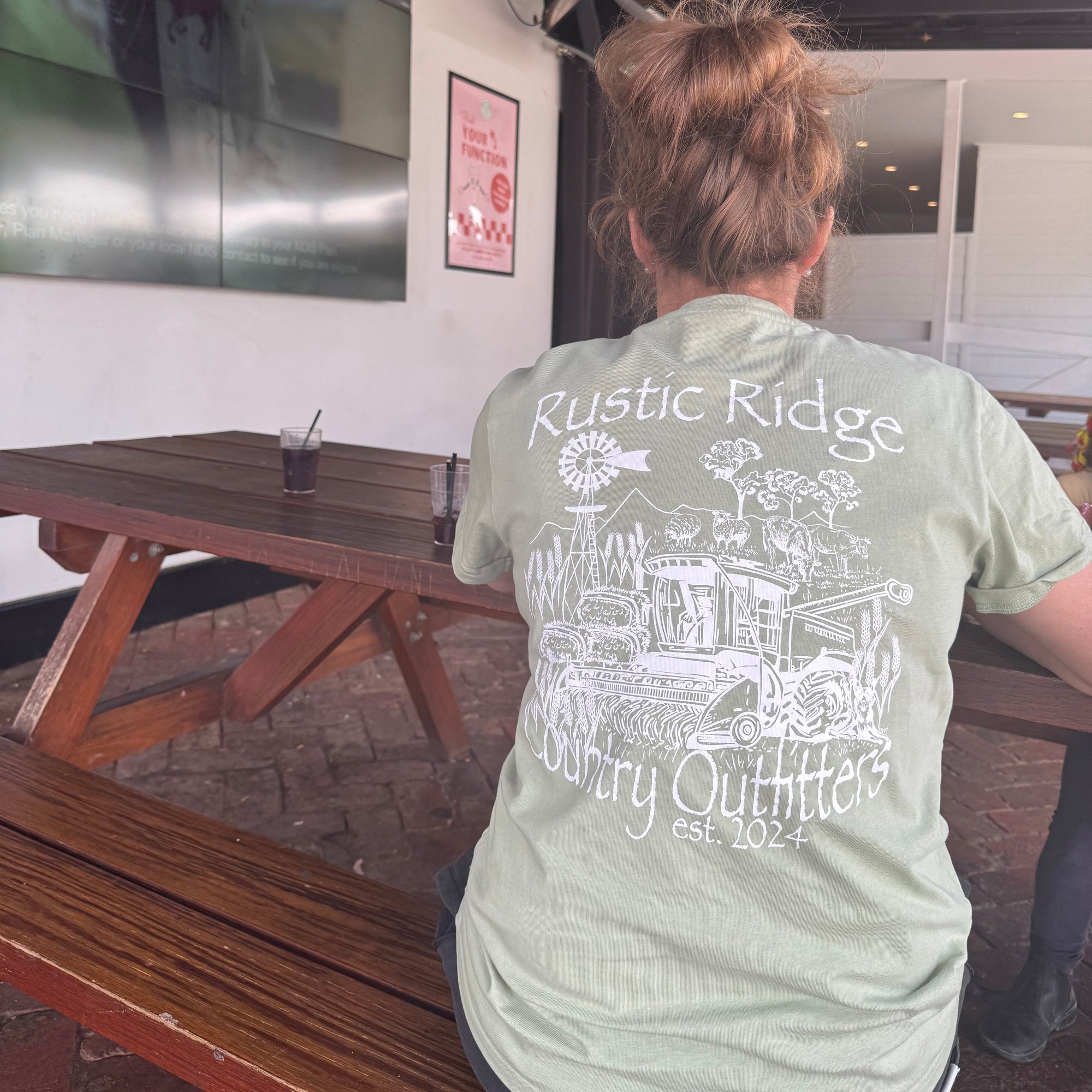 Person wearing a light green shirt with a graphic design, standing at a table with a laptop.