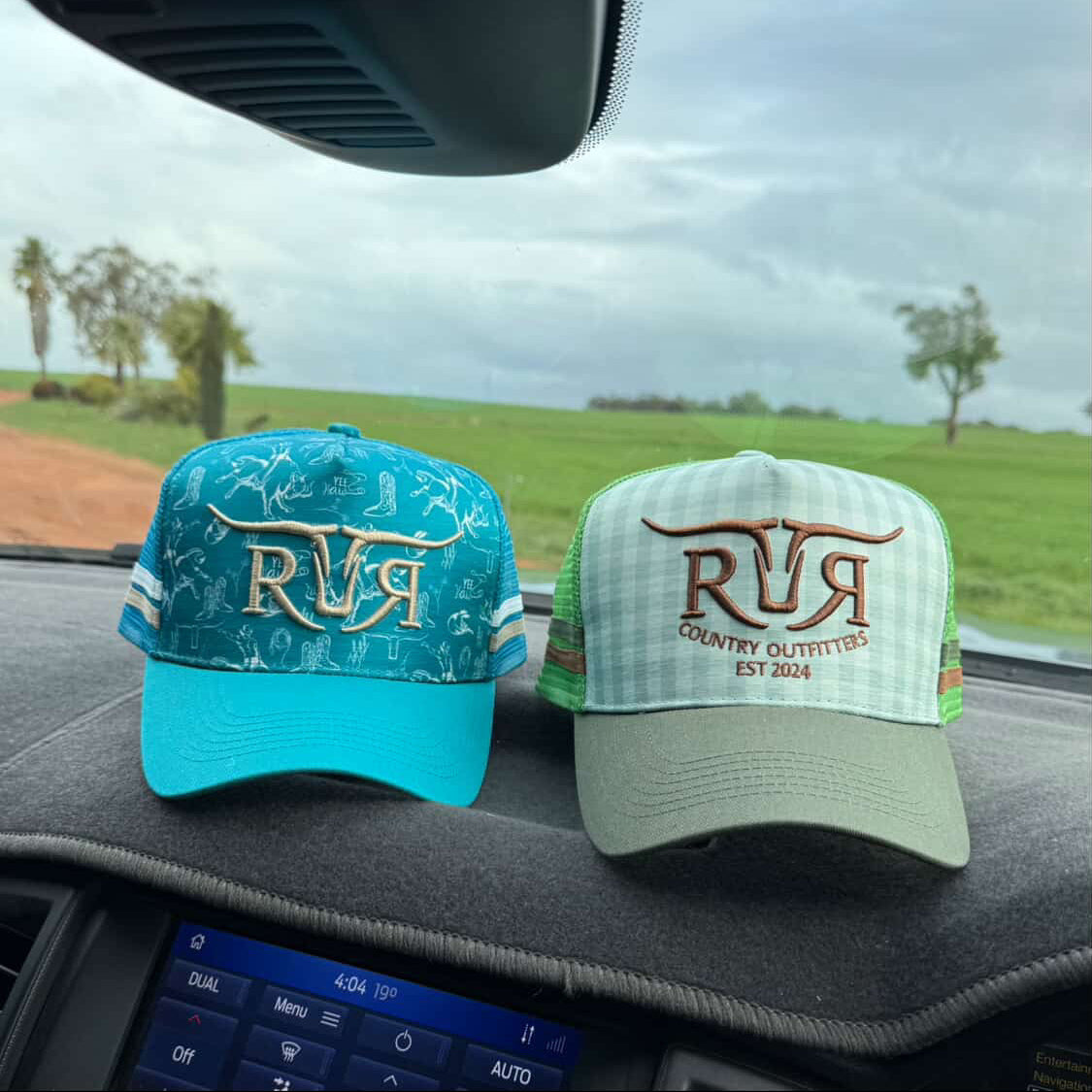 Two hats with 'RR' branding on a car dashboard with a scenic background.