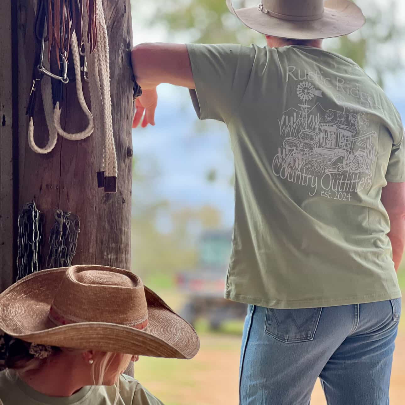 Two people wearing cowboy hats with a rustic setting and 'Rustic River Country Outfitters' shirt.