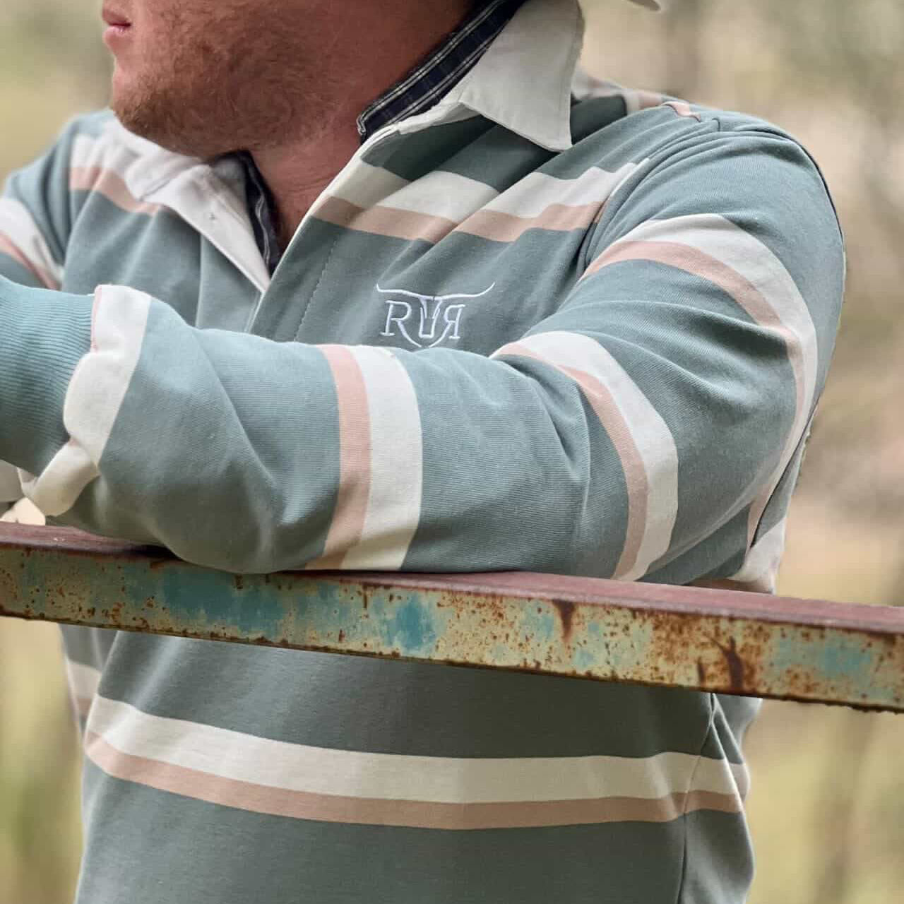 Person wearing a striped shirt with a brand logo, holding a rusty metal bar outdoors.