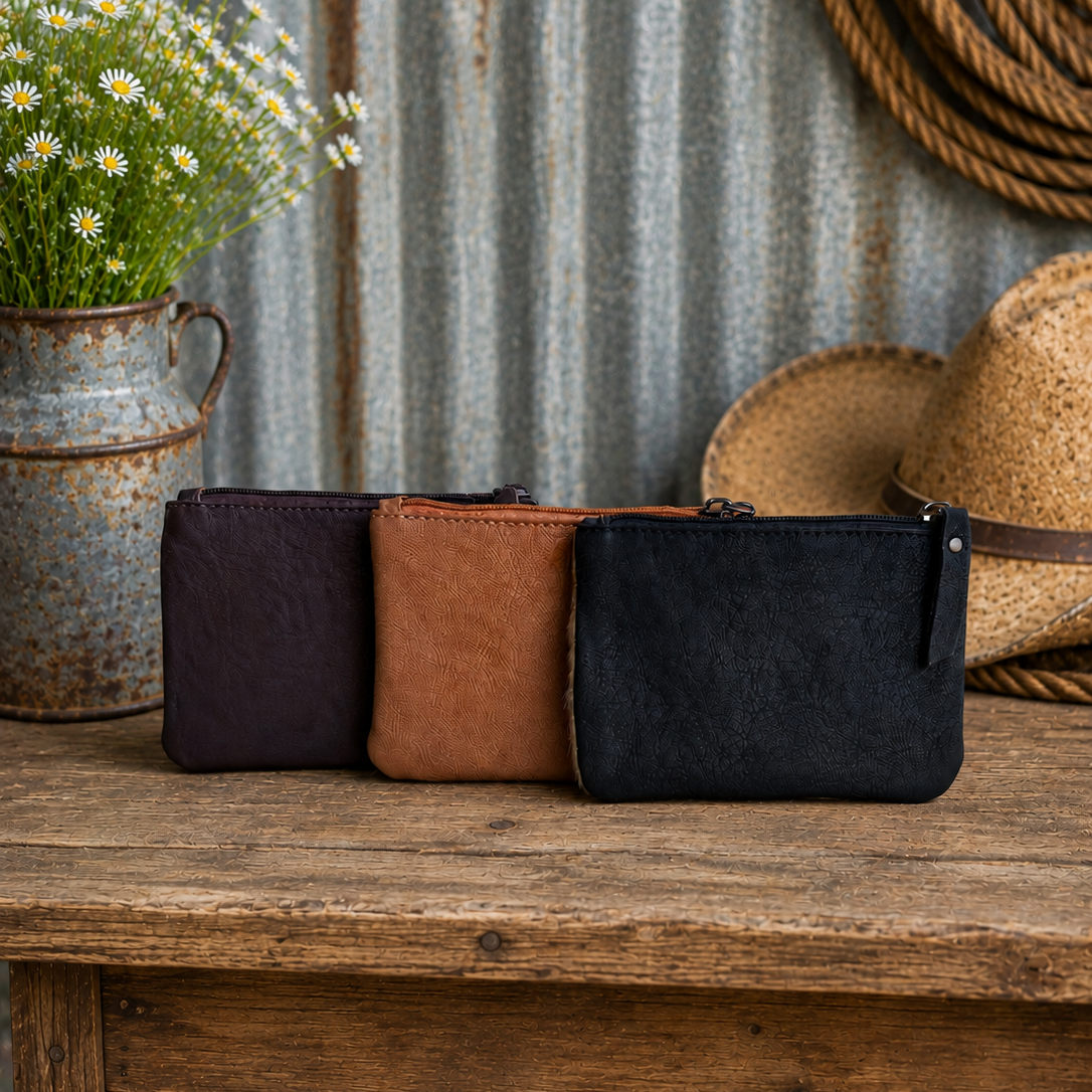 Three leather pouches in brown, black, and tan on a wooden table with a rustic background.