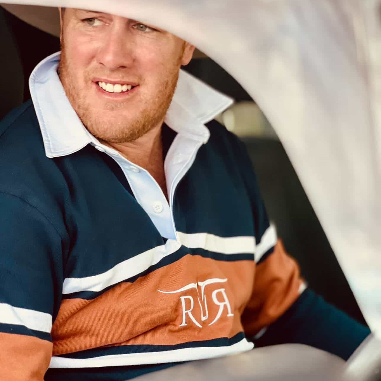 Man wearing a striped polo shirt with a logo, sitting inside a vehicle.