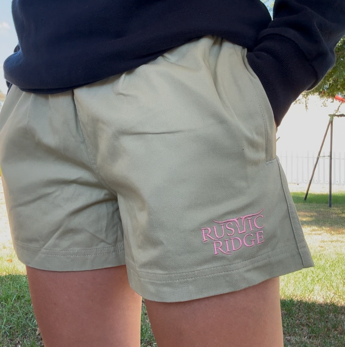 Person wearing a sweater and shorts with text, standing outdoors.