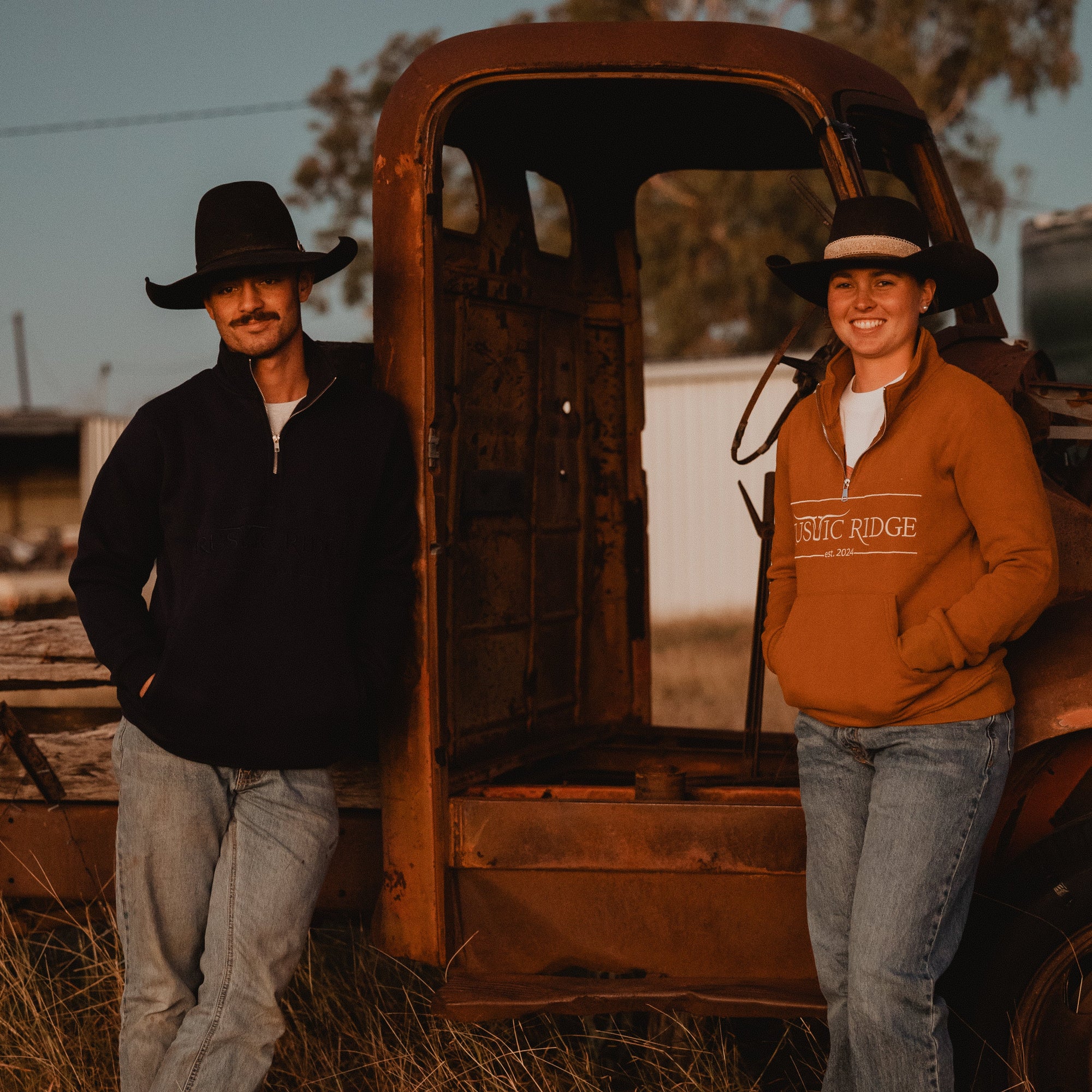 Two people standing next to an old, rusted truck in a field.