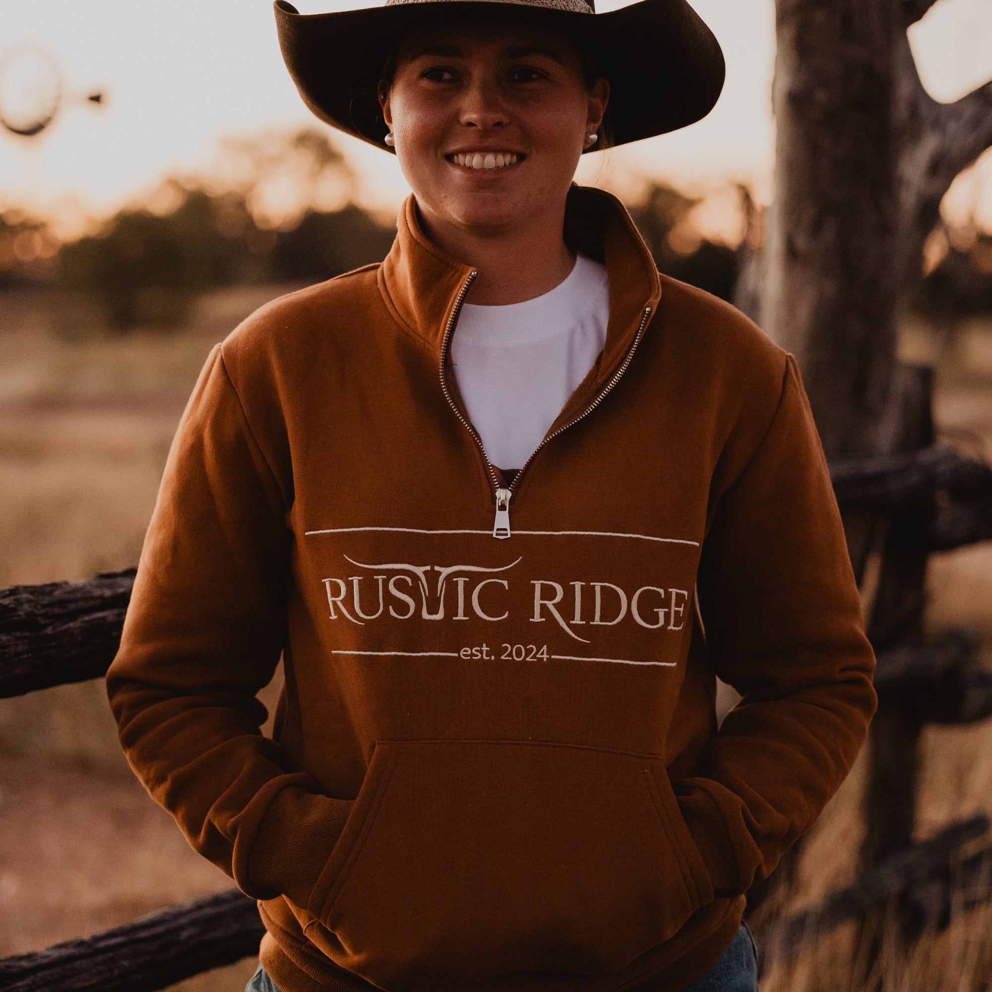 Person wearing a brown sweatshirt with 'Rustic Ridge' text, standing outdoors near a wooden fence.