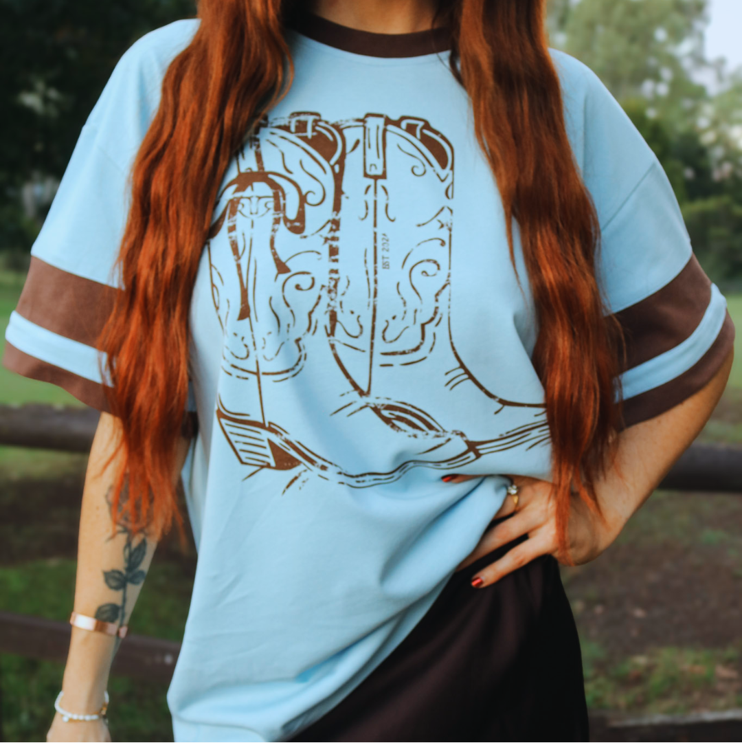Person wearing a light blue t-shirt with brown graphic design outdoors