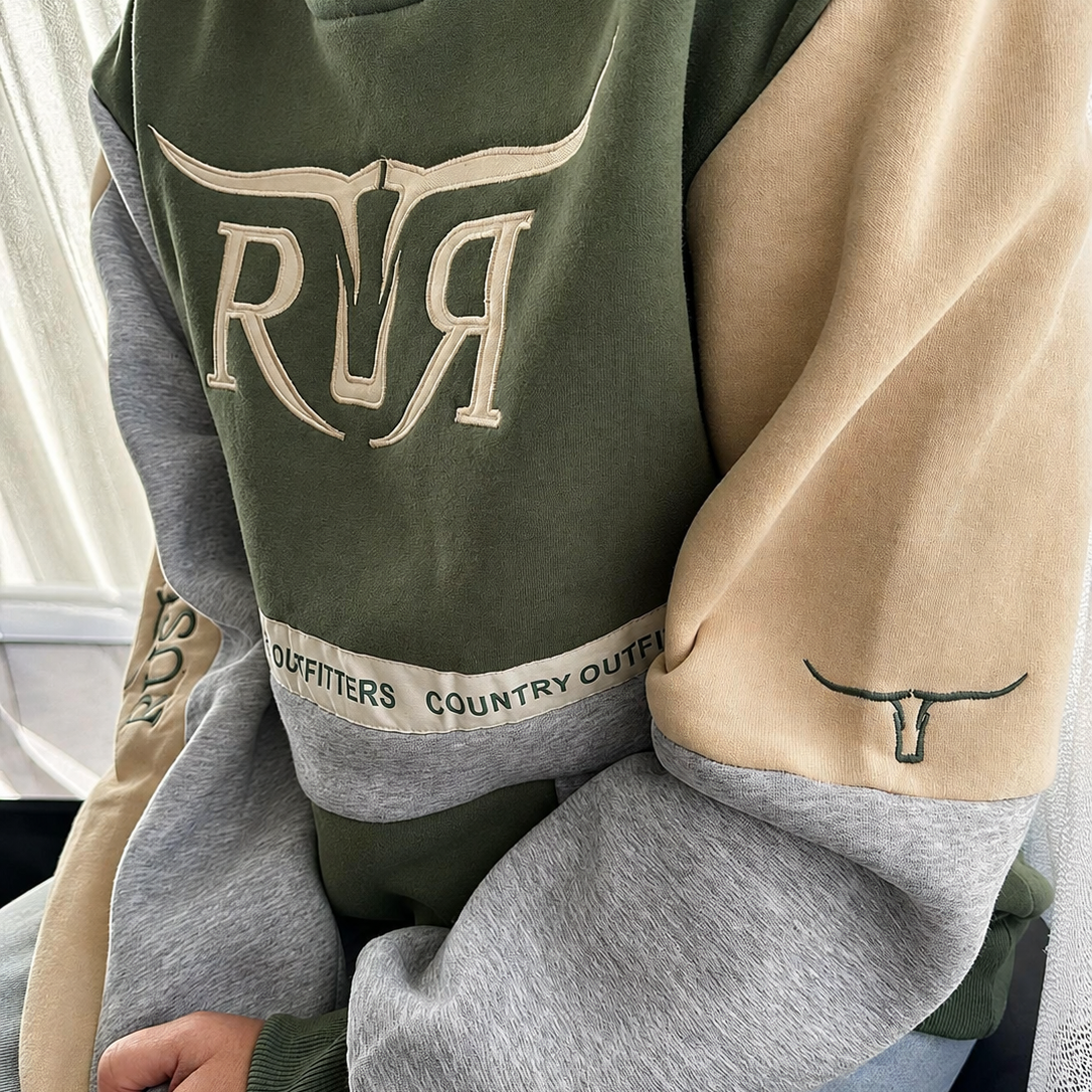 A person wearing a color-blocked crewneck sweatshirt with olive green, beige, and heather gray panels. The sweatshirt features a large beige 'RR' graphic on the chest, a beige longhorn logo on the sleeve, and a beige horizontal stripe near the hem with the text 'COUNTRY OUTFITTERS'.