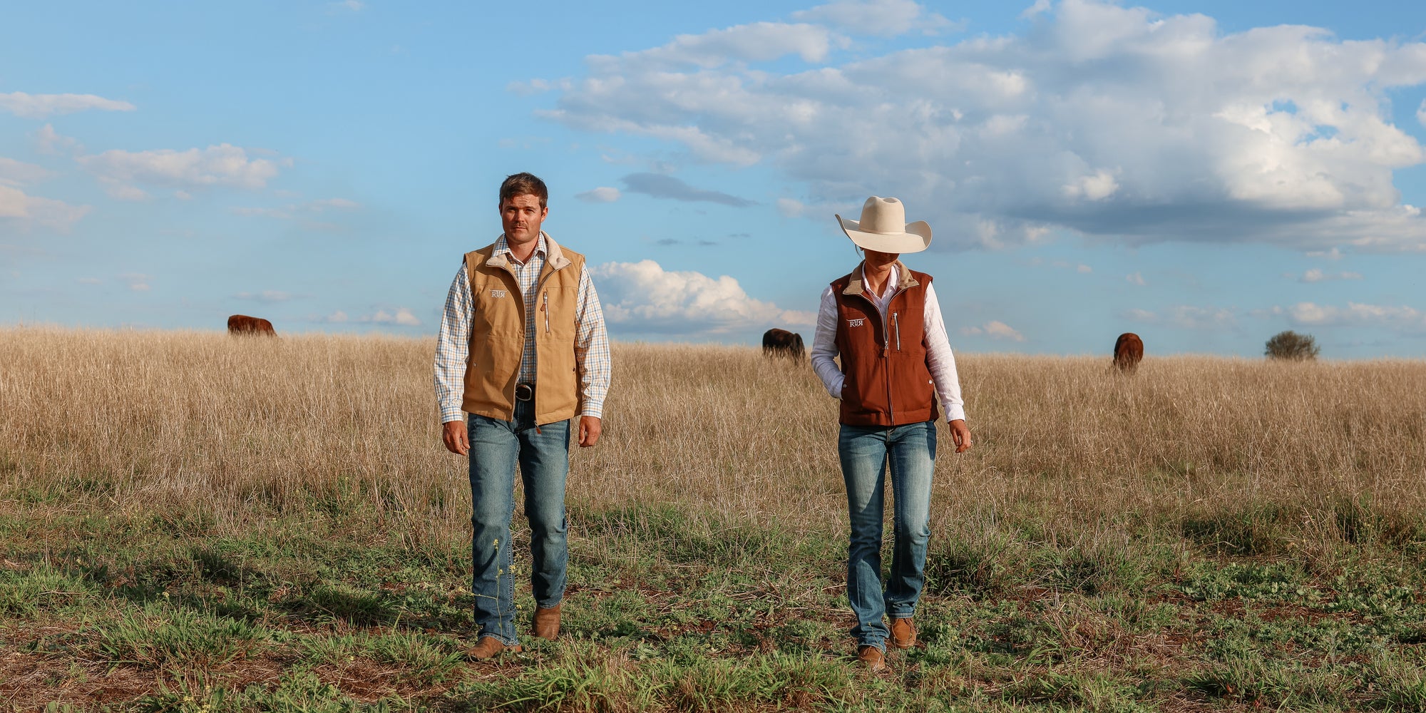 Two people in a field wearing cowboy hats and vests.