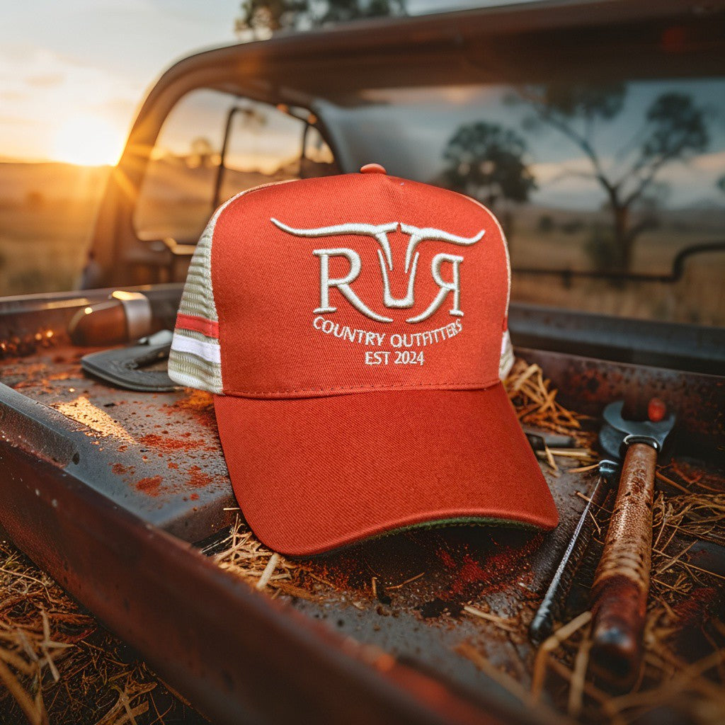 Rust cap with 'RR Country Outfitters' logo on a truck bed with tools at sunset.