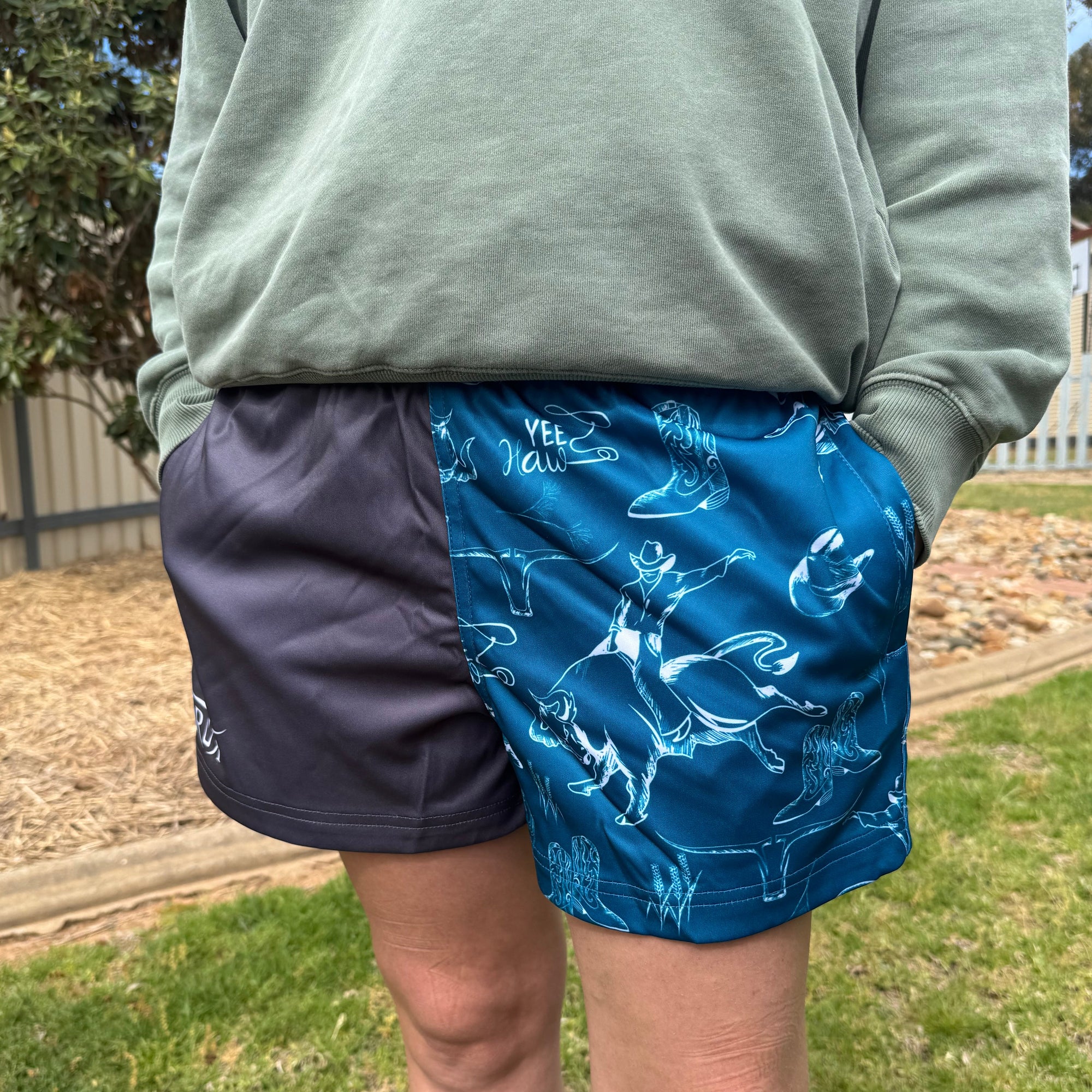 Person wearing a green shirt and blue patterned shorts outdoors on a grassy area.