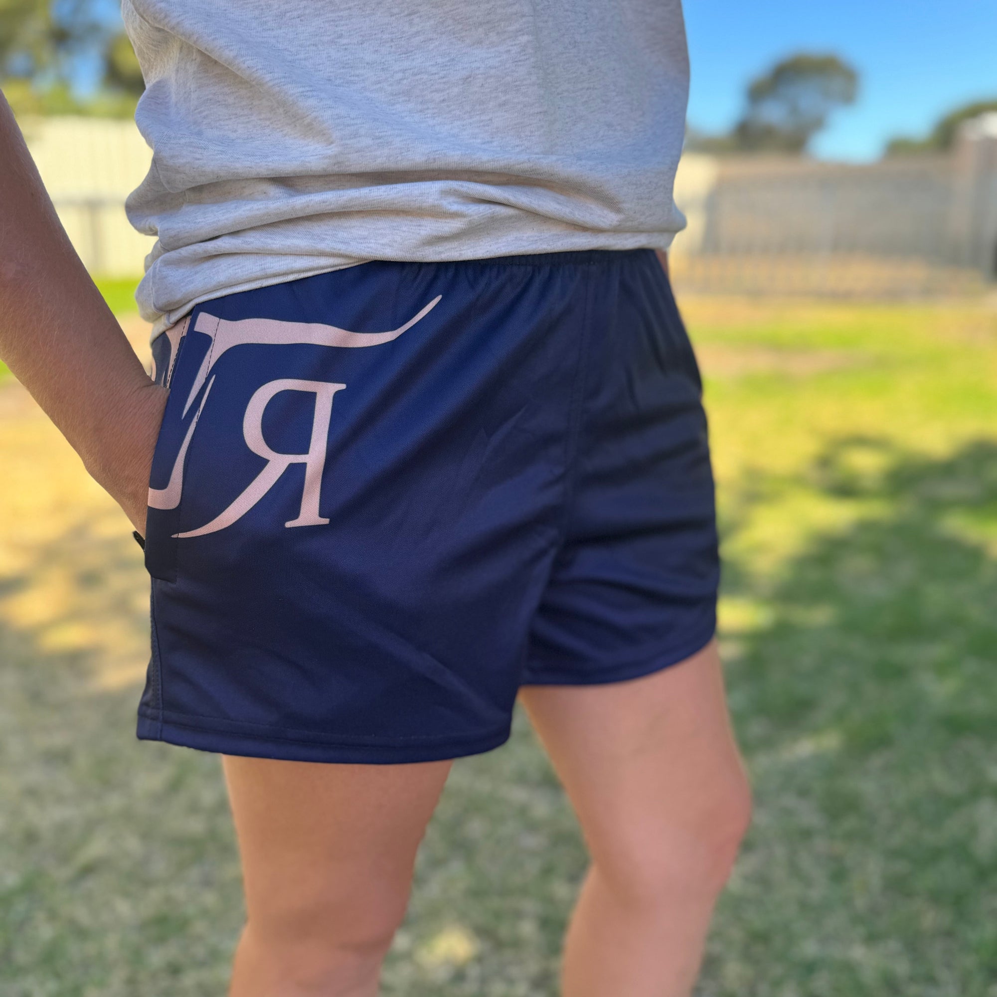 Person wearing navy shorts with a logo, standing outdoors on grass.