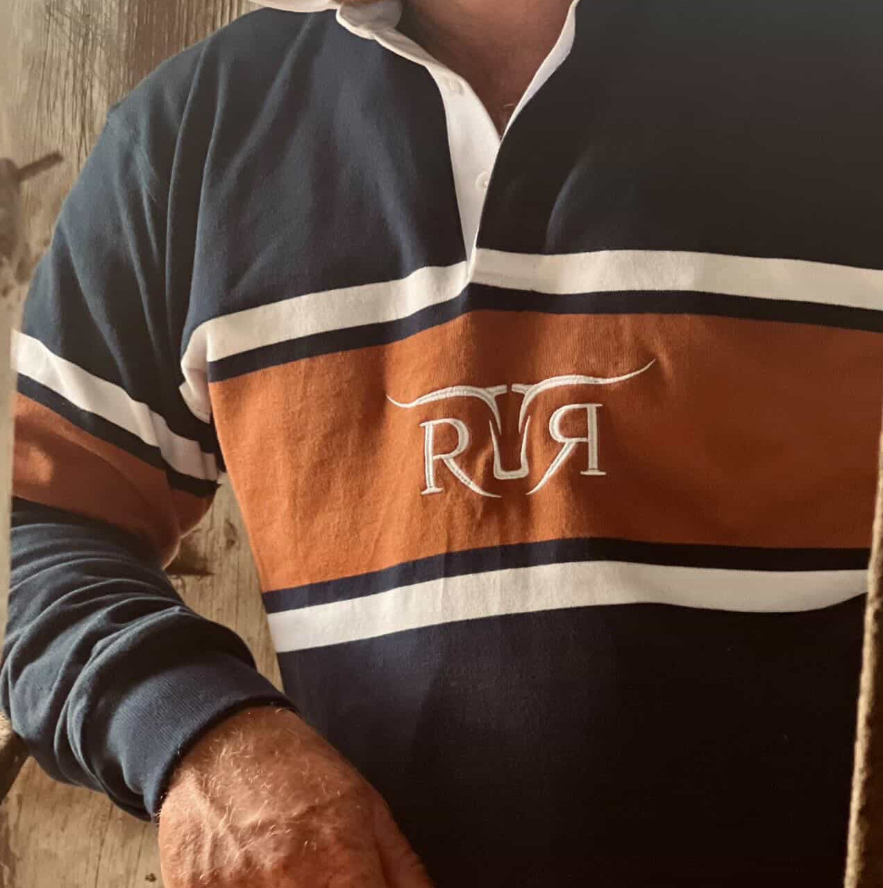 Person wearing a rugby jersey with 'RR' logo against a wooden background