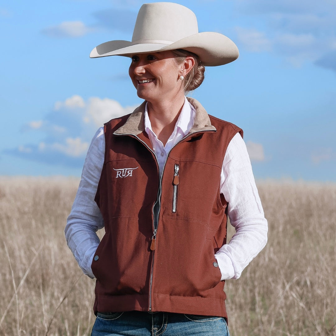 Person wearing a brown vest with 'RR' logo, white shirt, and beige cowboy hat in an open field.
