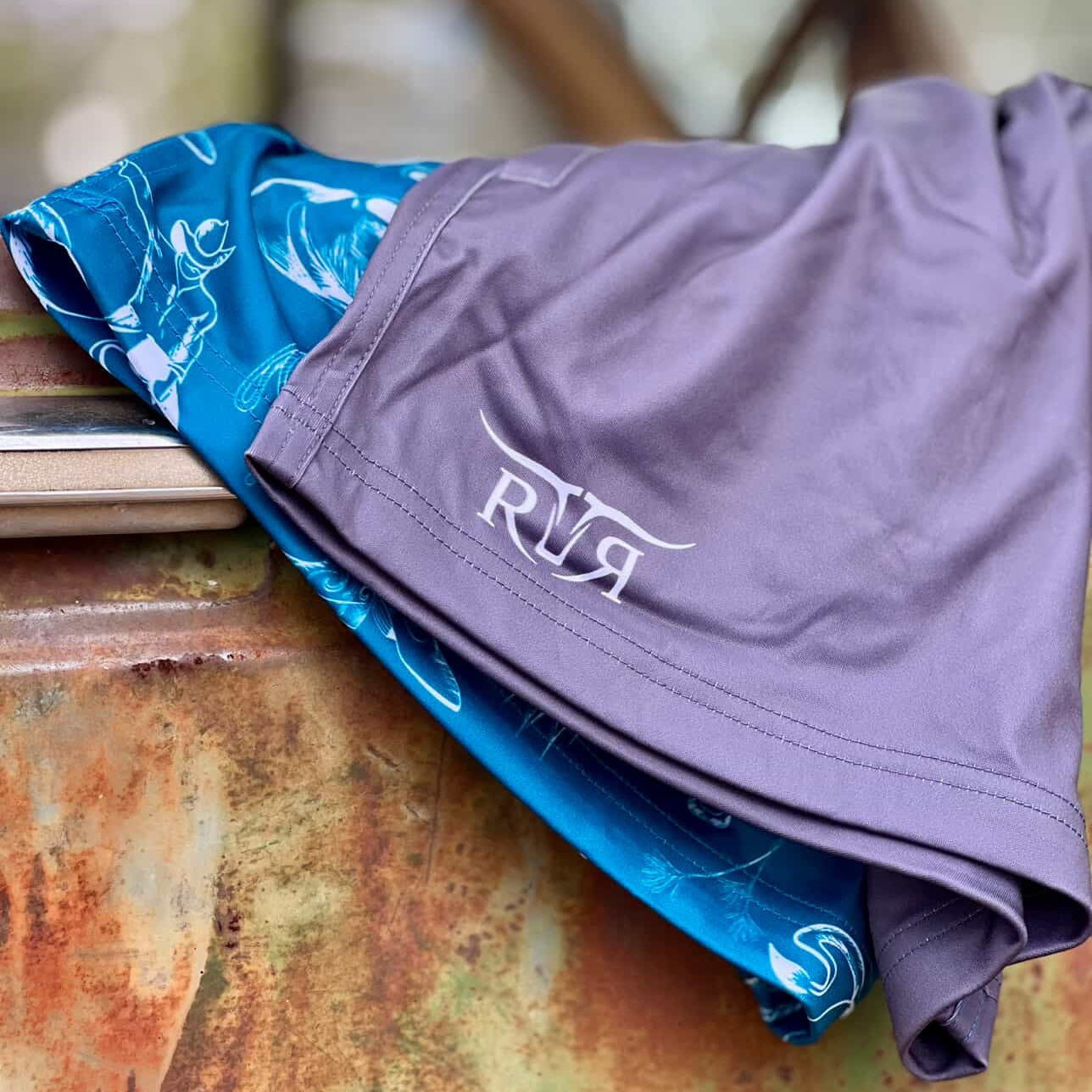 Purple shorts with a logo and blue shorts with a pattern on a wooden surface.