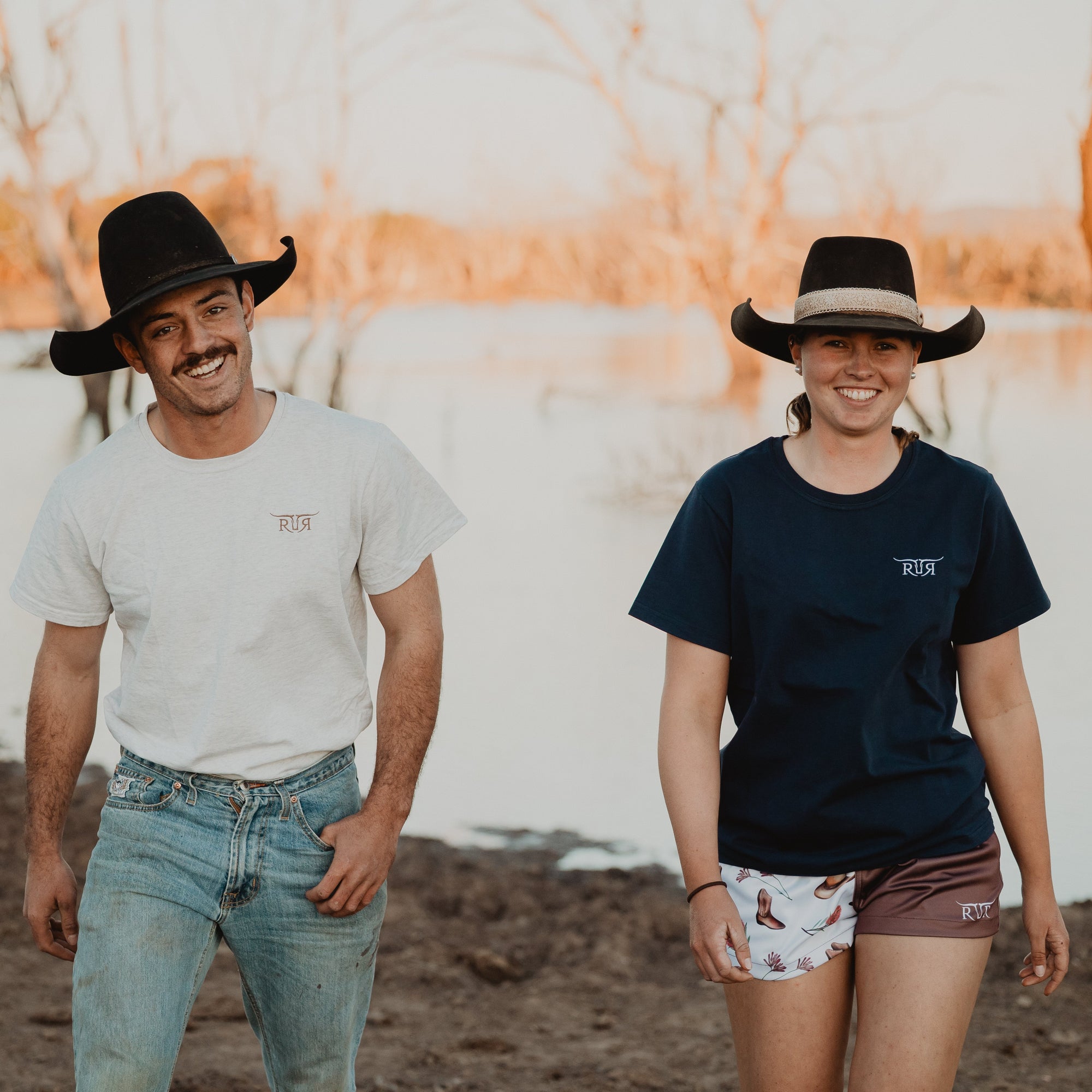 Two people wearing cowboy hats standing in a field with a sunset in the background