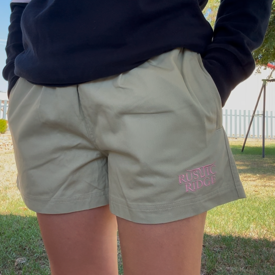 Person wearing khaki shorts with 'Rustic Ridge' logo in a grassy area.