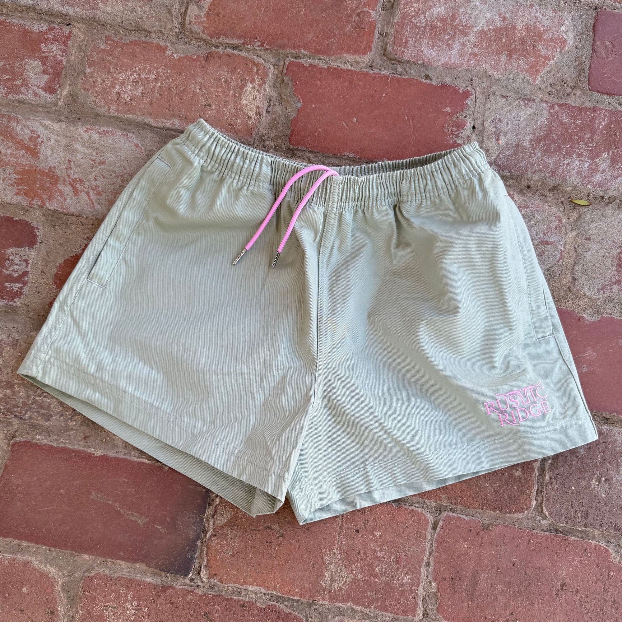 green shorts with a pink drawstring on a brick surface