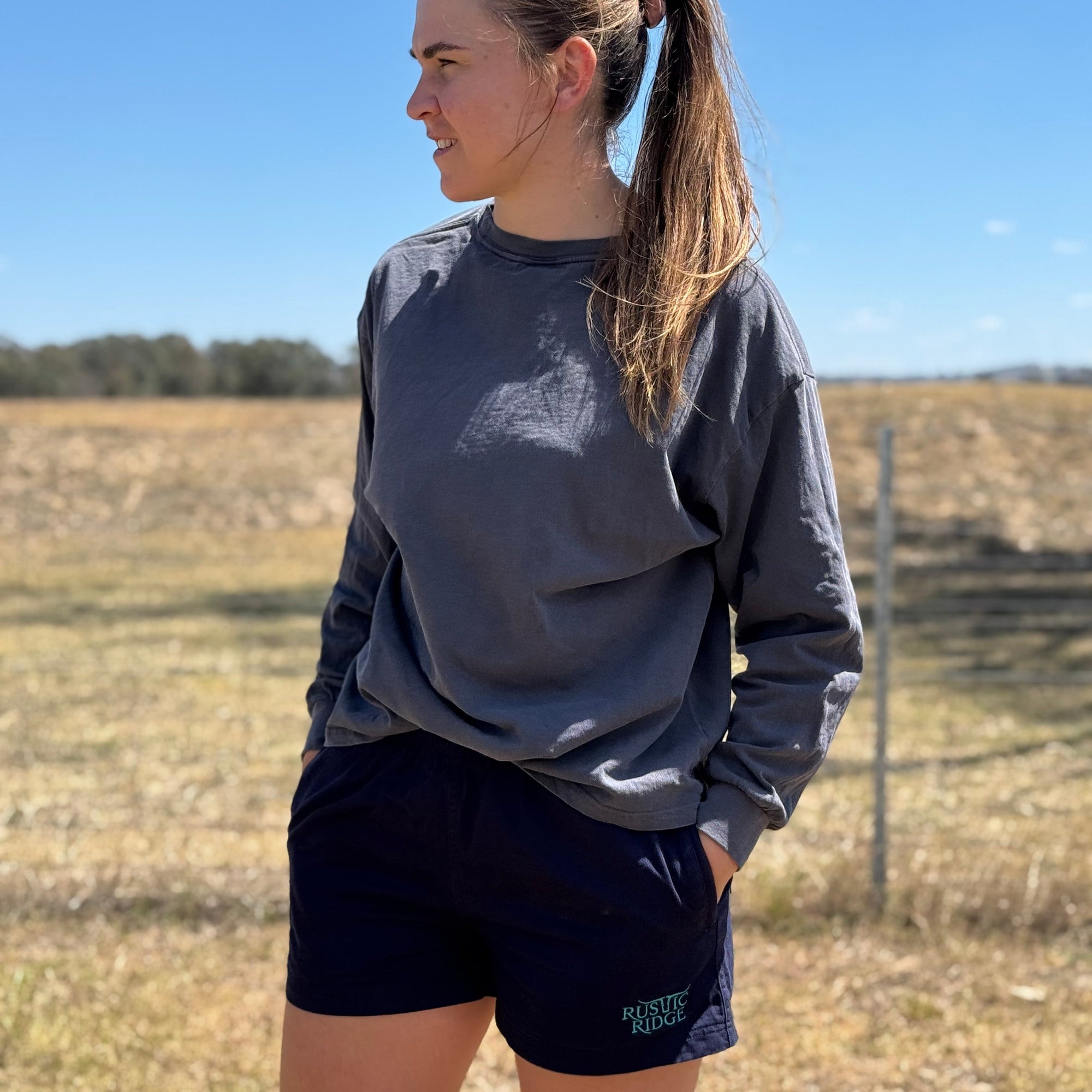lady wearing blue work shorts, standing in a paddock. 