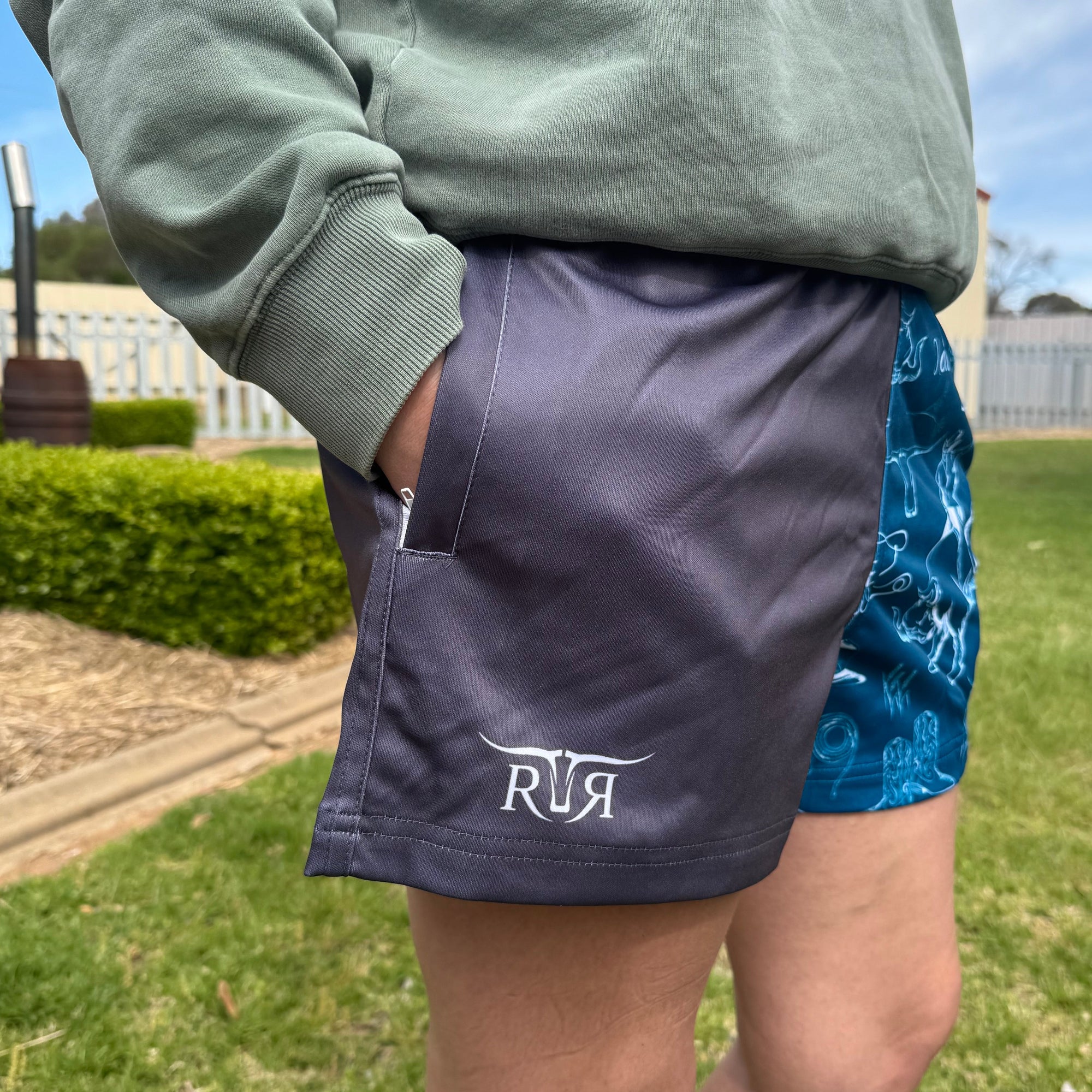 Person wearing a green sweatshirt and purple shorts with a logo, standing outdoors on grass.