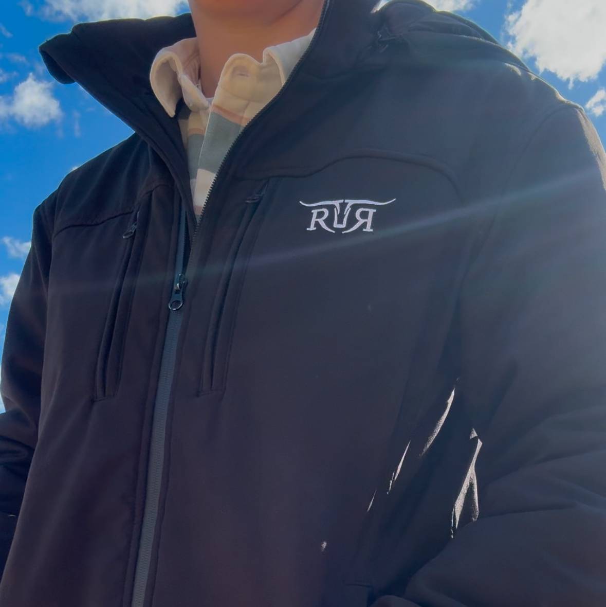 Person wearing a dark jacket with 'RR' logo against a blue sky