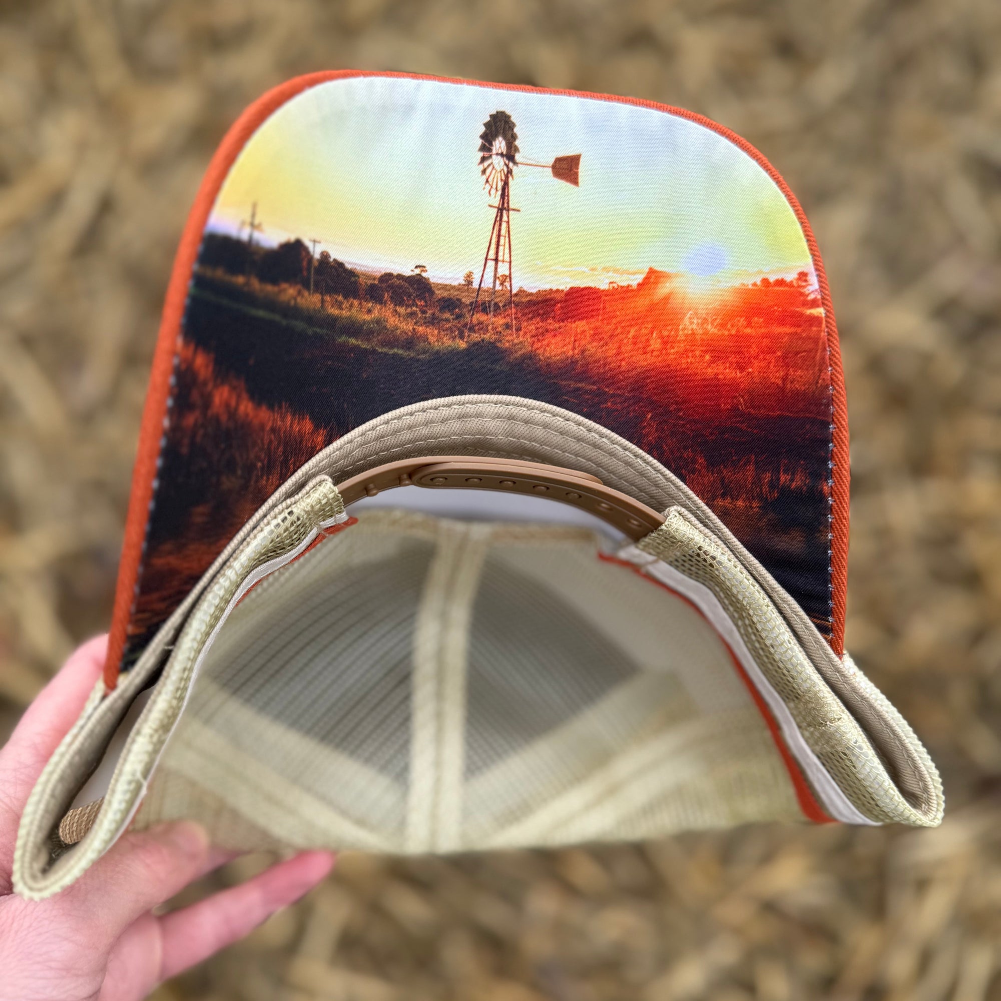 Cap with a printed design of a windmill and sunset held against a straw background