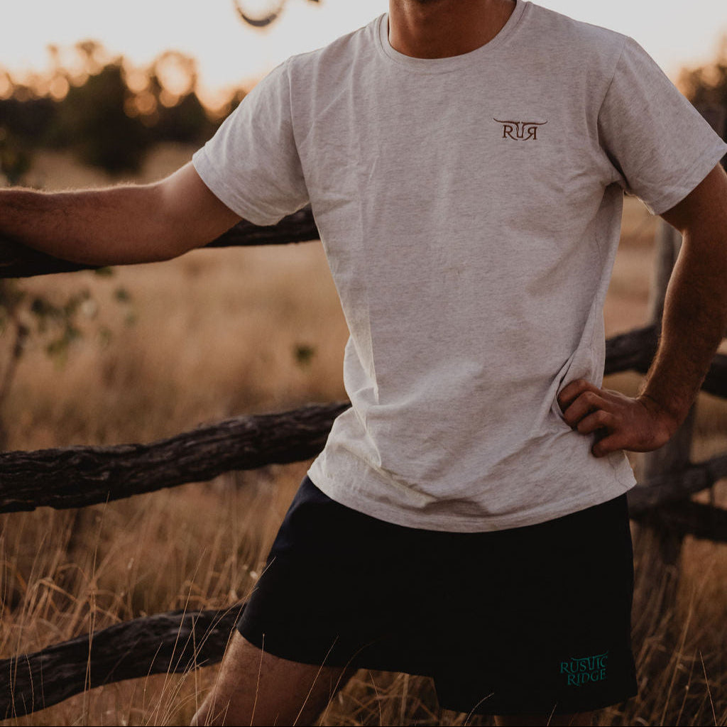 Man wearing a cowboy hat and casual clothing standing in a field with a sunset or sunrise in the background.