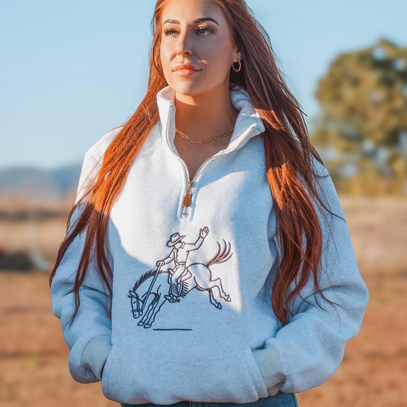 Woman wearing a light gray pullover with a graphic design outdoors