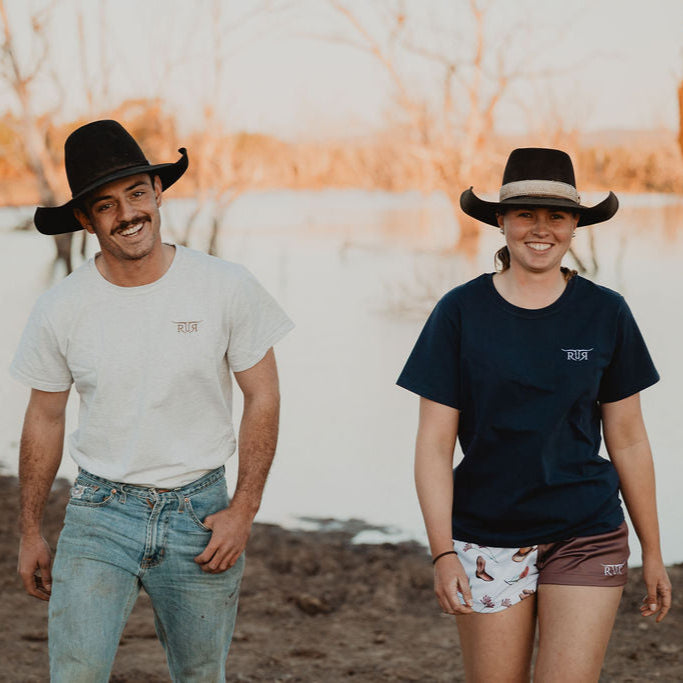 Two people wearing cowboy hats standing in a field with a sunset in the background