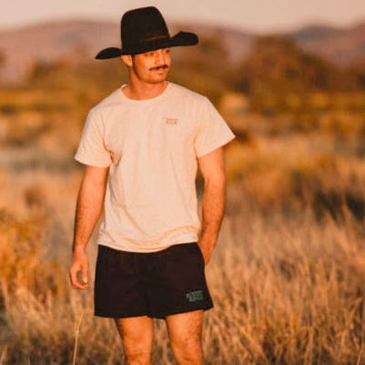 Man wearing a cowboy hat and casual clothing standing in a field with mountains in the background